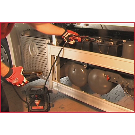 Person schließt Starthilfe an LKW-Batterie an. Rote Handschuhe, schwarze Kabel, Mercedes-Stern erkennbar.